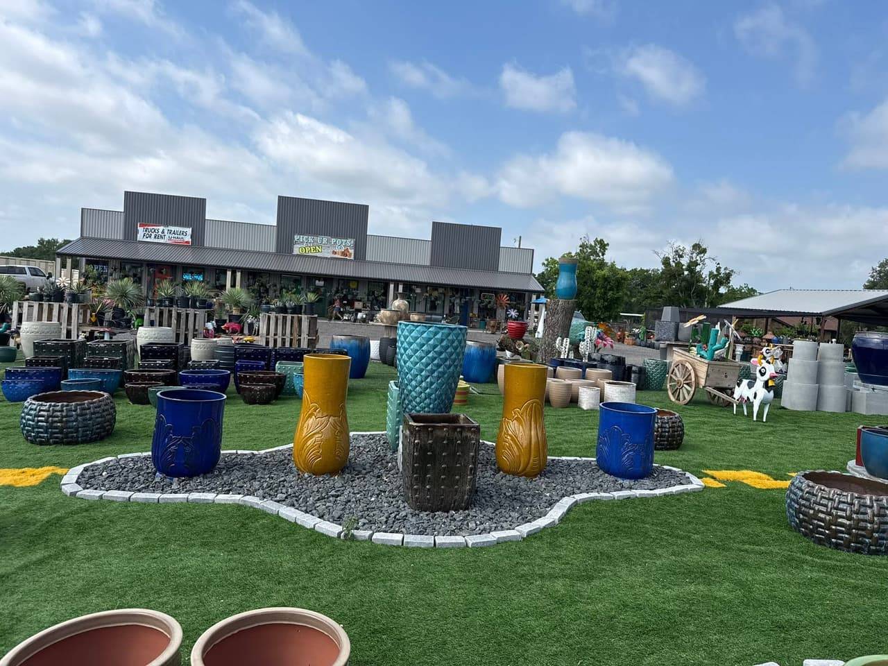 Tall glazed blue and gold pots on a gravel island in front of the Pick Ur Pots storefront in Stephenville, TX